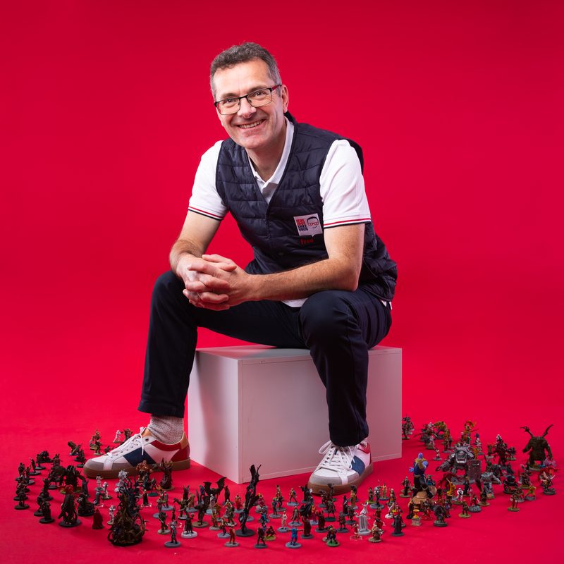 Frédéric assis, souriant, entouré de dizaines de figurines de jeu peintes à la main